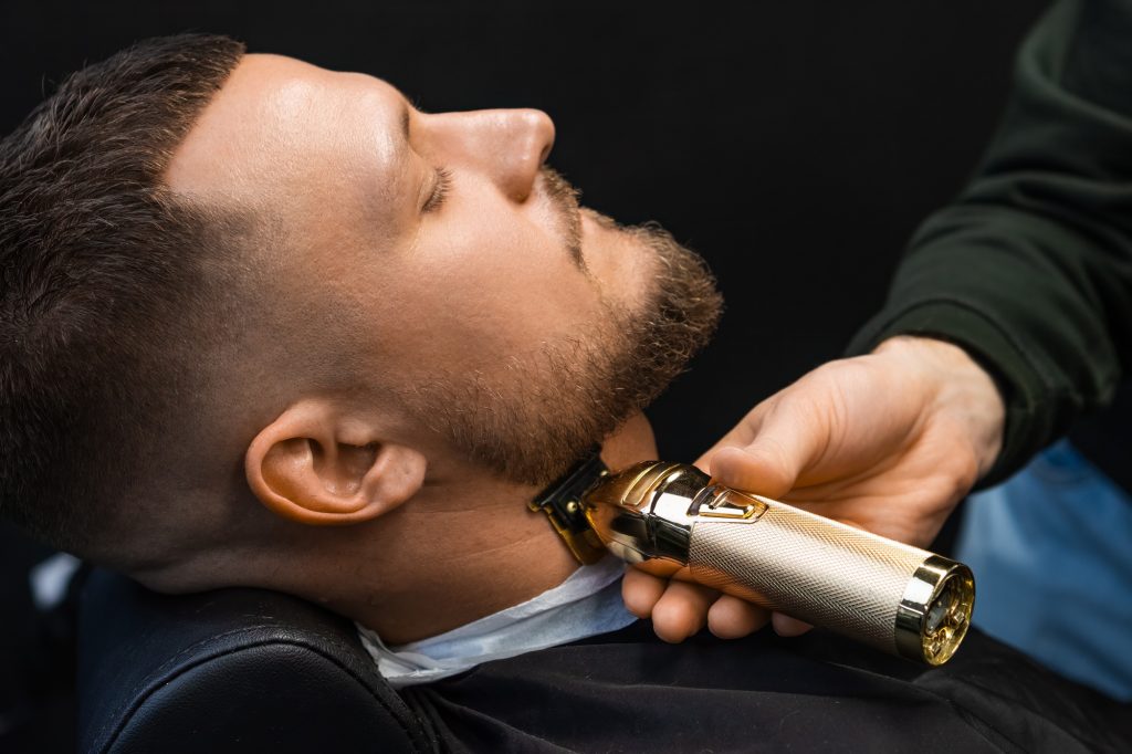 The barber uses an automatic trimmer to cut the client's beard at the barbershop.